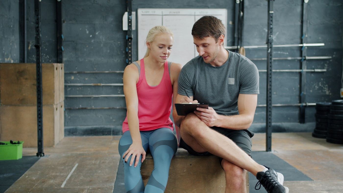Two people reviewing a plan on a tablet beside gym equipment.