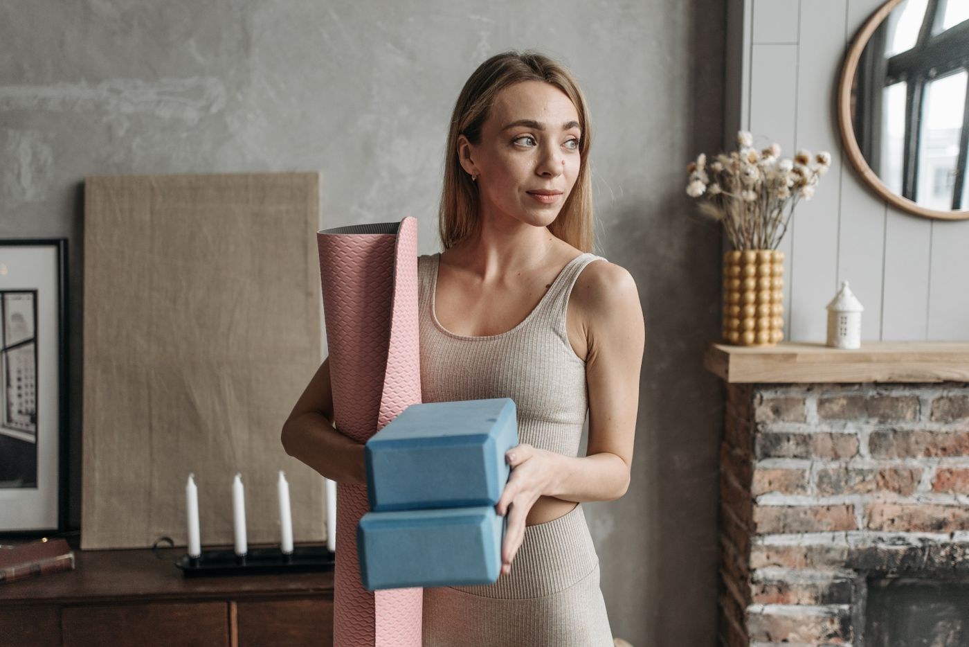 A woman holding a rolled mat and blocks in a living room.
