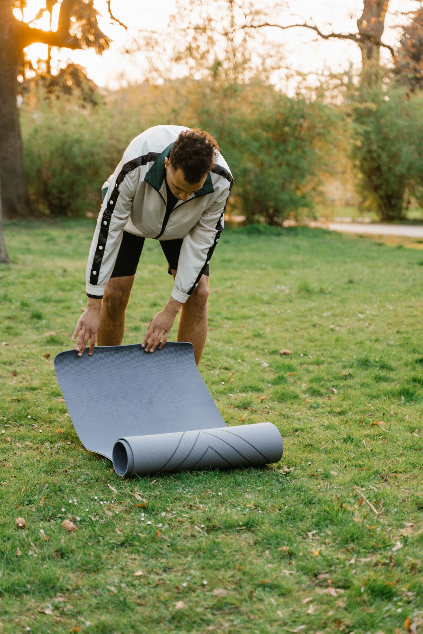 A man laying out a mat on grass before an outdoor session.