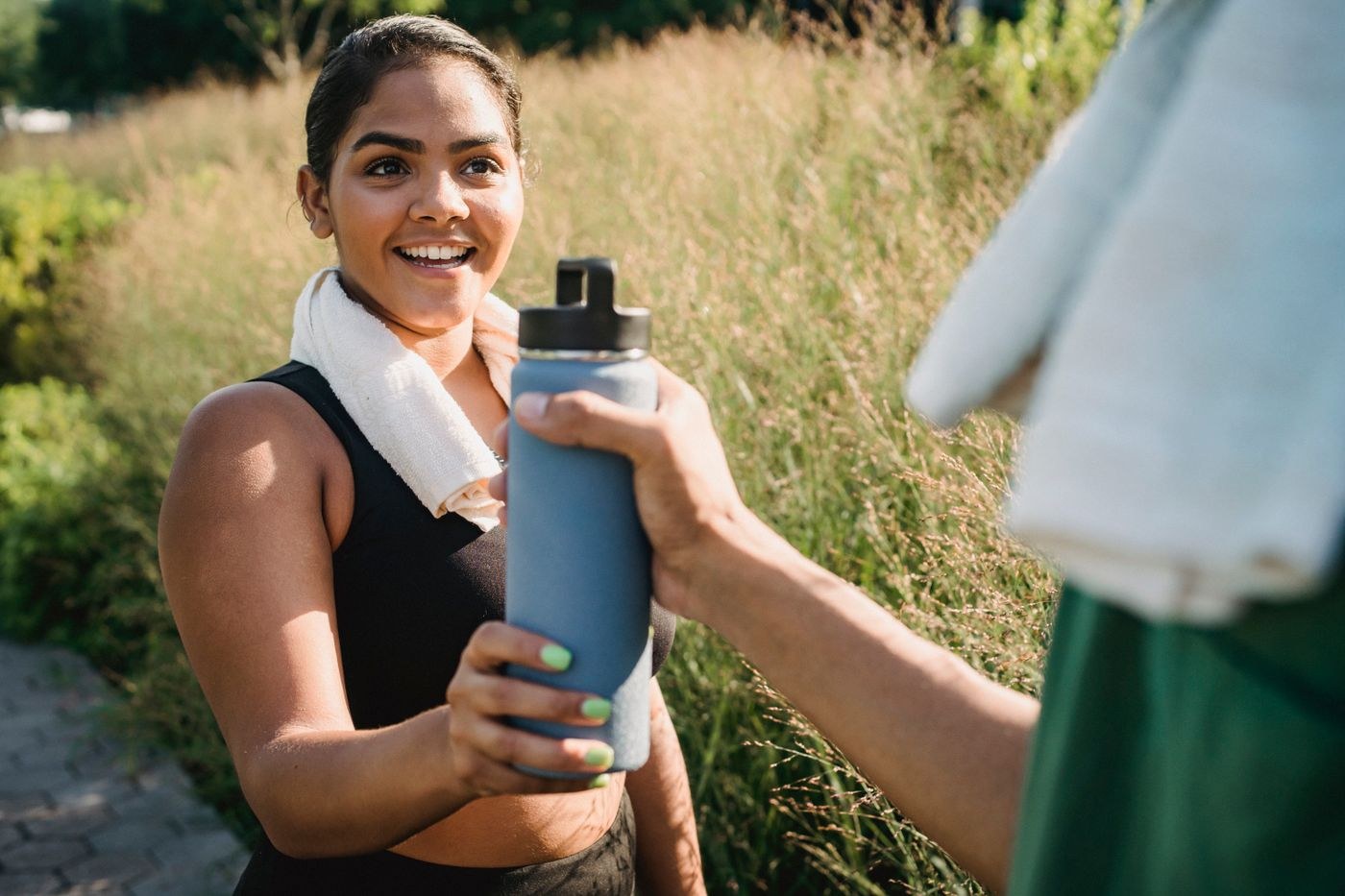 A woman accepting a refillable water bottle during an outdoor exercise break.
