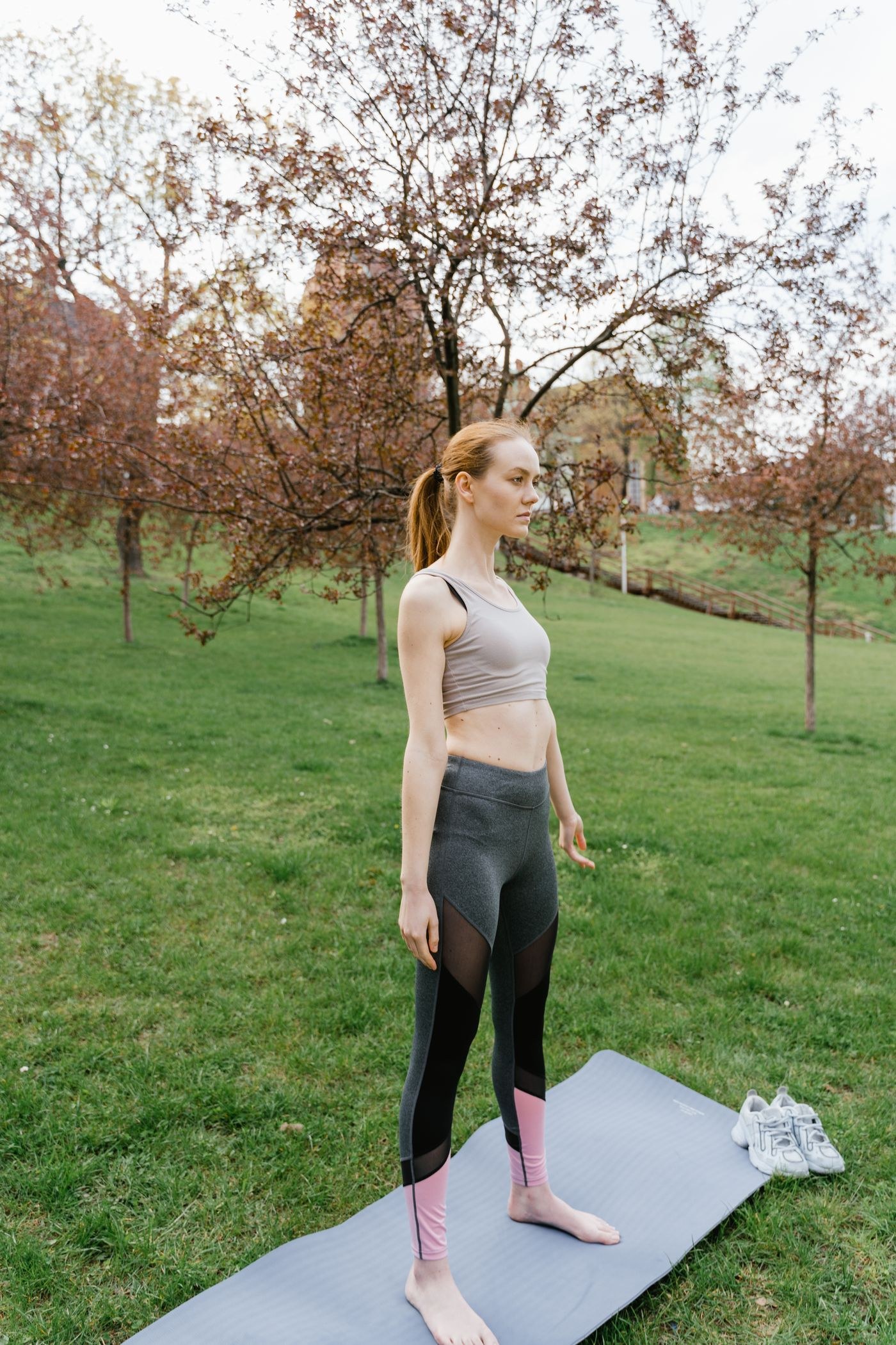 A woman standing quietly on an exercise mat in a park.