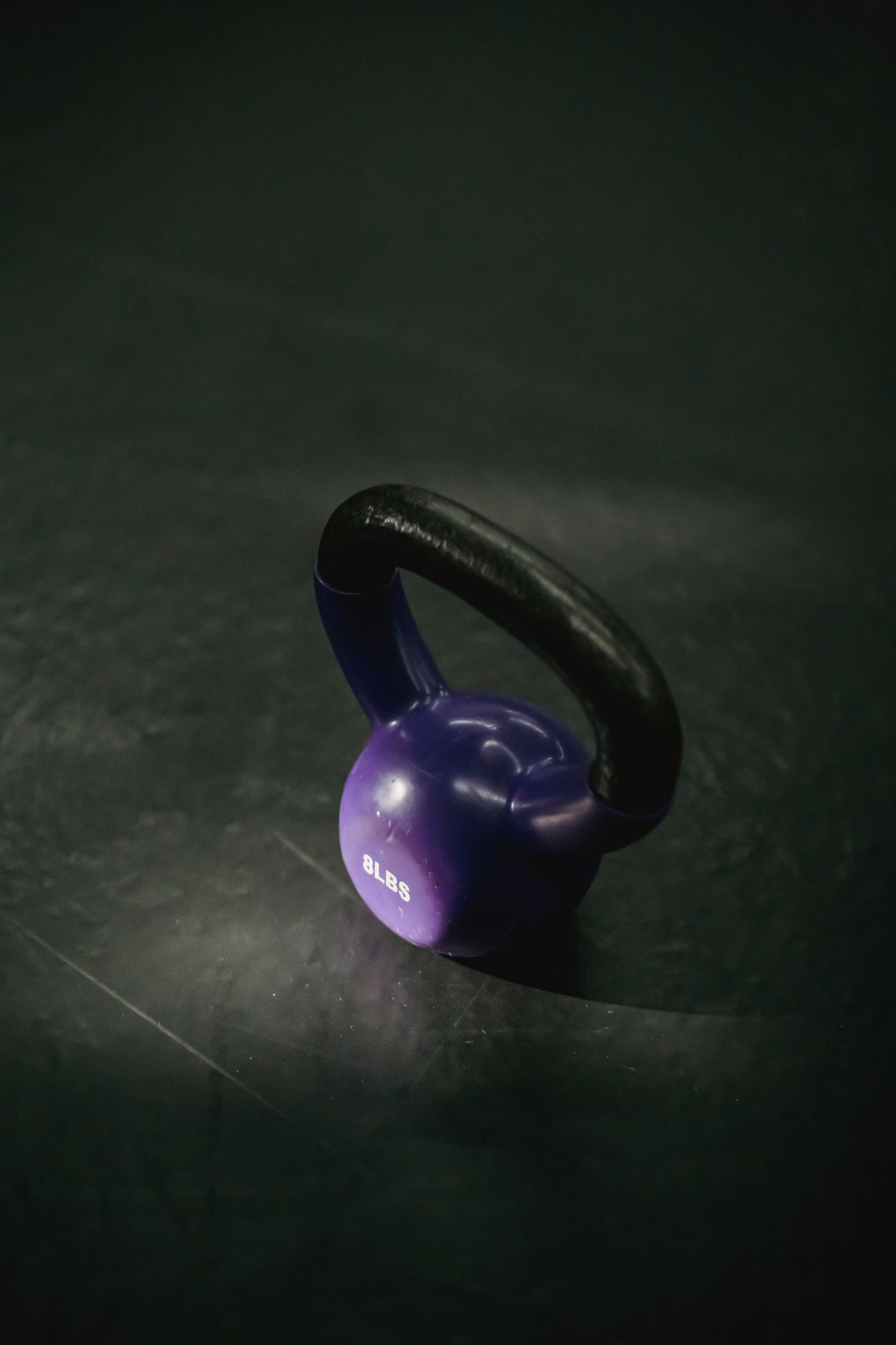 A purple kettlebell with a black handle on a gym floor.
