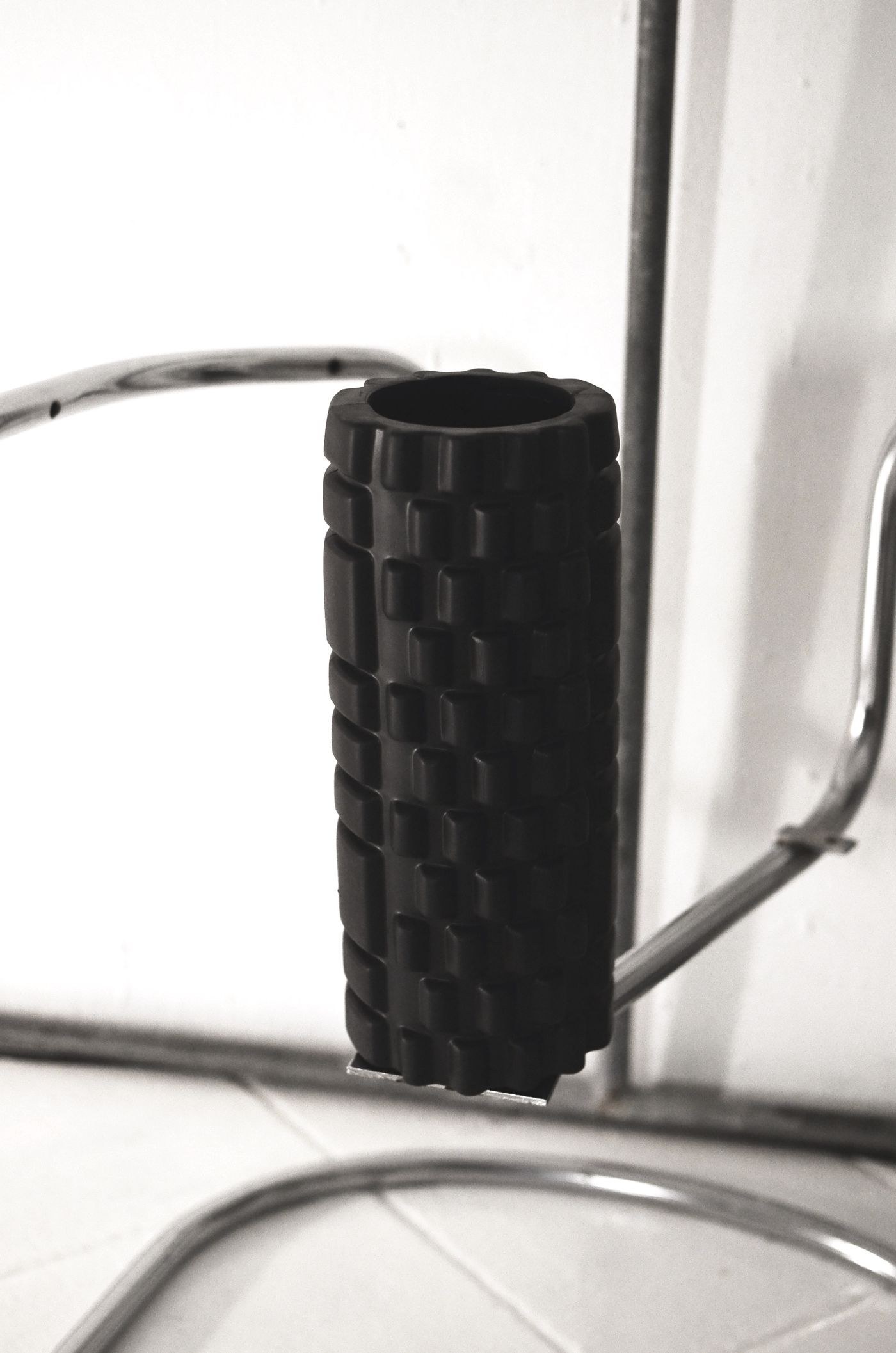A black textured foam roller resting on a metal stand.