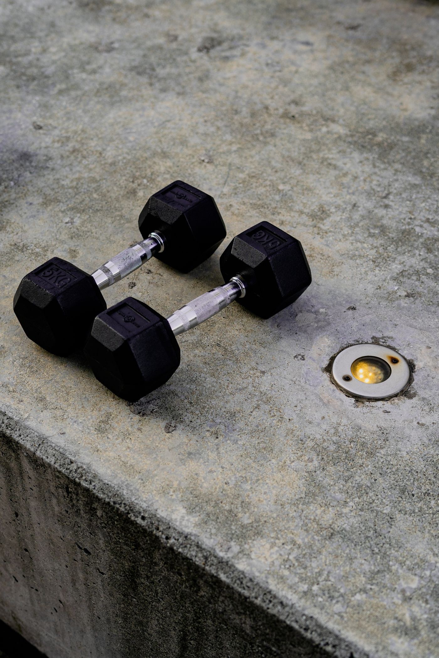 Two black hex dumbbells resting on a concrete surface for inspection.
